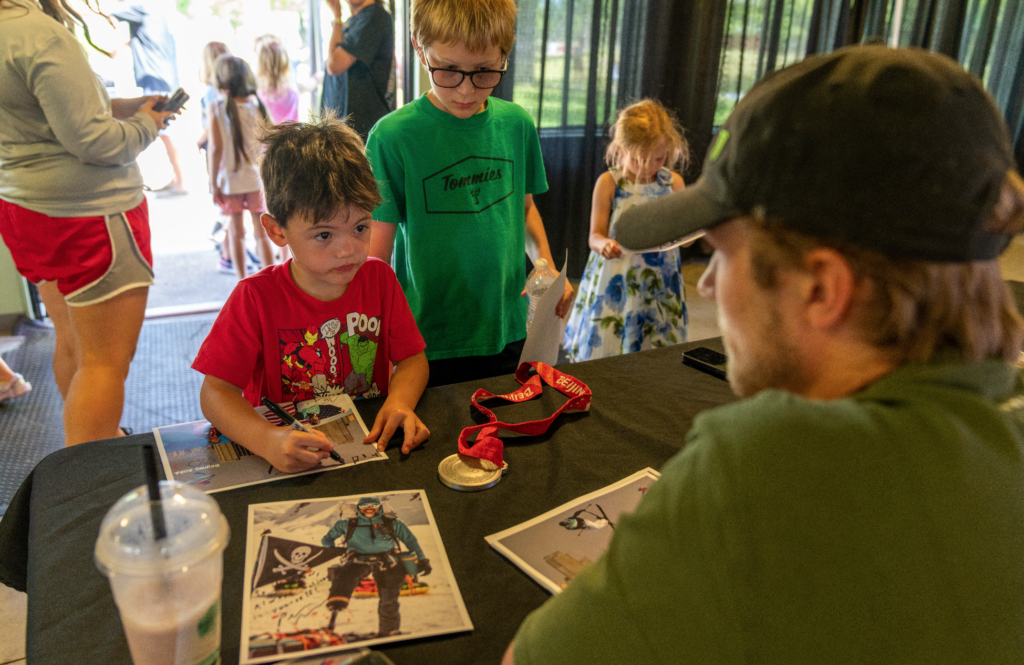 A man and two children sit at a table, looking at a picture of another man displayed in front of them